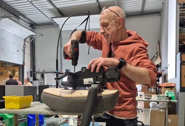 Homme debout qui assemble un si&egrave;ge avec une perceuse, le Hapo AR soutient son bras